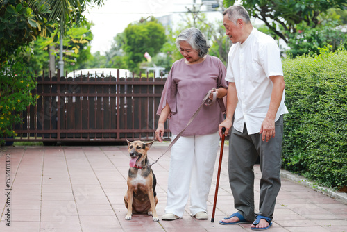 Asian senior couple walking their dog in front of their house. Pet concept. Keeping a dog helps improve the health of the elderly.