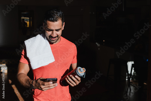 Latin young man using mobile phone after exercising or doing workout session at home in Mexico Latin America, hispanic young people in wellness concept