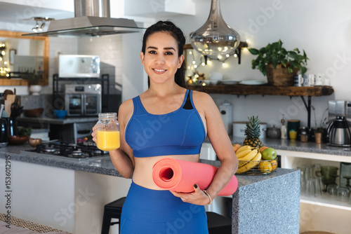 portrait of young latin woman doing exercise and workout at home drinking orange juice and holding a yoga mat in Mexico Latin America, hispanic female in wellness concept