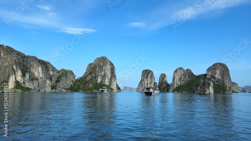 Towering limestone cliffs frame a serene channel of emerald water in Ha Long Bay, Vietnam, beneath a blue sky with soft clouds.