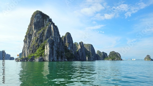 Towering limestone islands rise dramatically from the emerald waters of Ha Long Bay, Vietnam, under a bright blue sky.