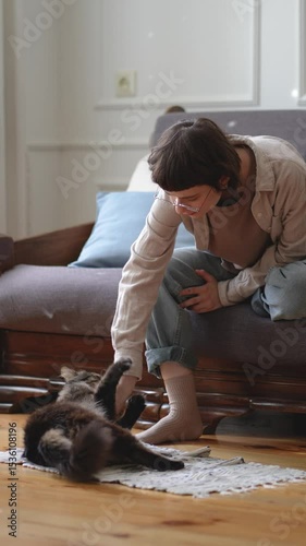 Woman playing with cat on floor as feline bites and scratches hand during playful battle interaction. Pet bond, animal fun activity energy, mutual enjoyment, claw marks on skin, games for healthy cat 