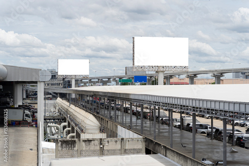Fototapeta Naklejka Na Ścianę i Meble -  Blank billboard signs over urban parking lot and elevated expressway background with cloudy sky in cityscape