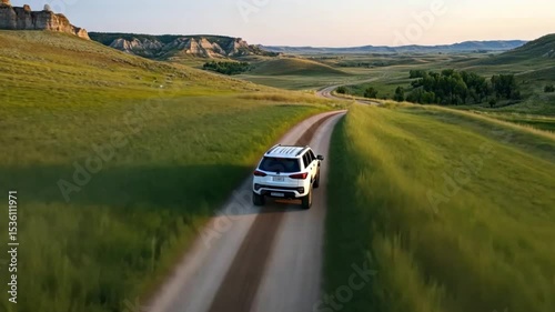 White SUV on Scenic Country Road, Grassy Hills, and Distant Cliffs at Sunset