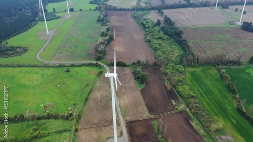 Wind turbine stands tall over lush green fields in rural area during daytime