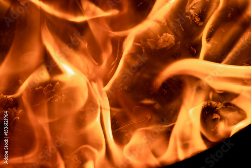 Close-up image of bright orange flames against a backdrop of black ash and burnt debris. A strong visual composition depicting the power, energy, and beauty of nature in the form of the fire element. 