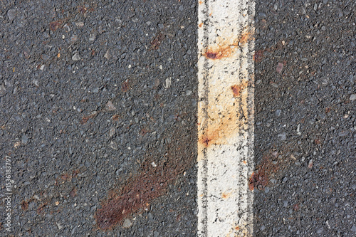 Asphalt road with a white painted line and rust stains close-up abstract textured background