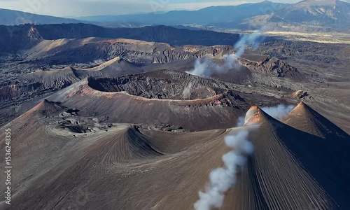 Aerial view of an active volcanic landscape with smoke rising from craters and surrounding mountains