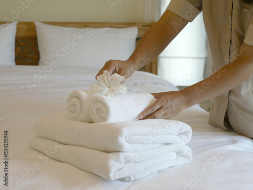 Hotel maid's hands place white flowers and towels on the bed in a luxury hotel room ready for guests who come to visit and want to rest