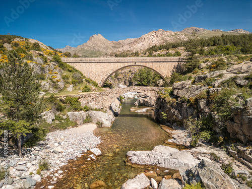The Ponte Altu bridge sits alongside an ancient genoise bridge at Albertacce on the Mediterranean island of Corsica passing over the crystal clear Golo river and with Monte Albanu in the distance