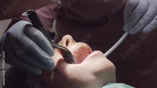 Doctor works on patient widely open mouth using suction tool during procedure. Woman jaw fixed stable allowing clear access for dental treatment