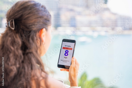 Young woman checking UV index on smartphone with high radiation alert. Mobile app warns to apply sunscreen before going outdoors