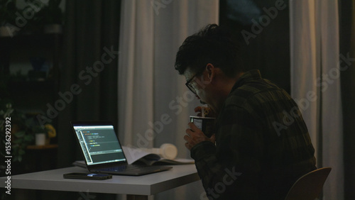 Billede på lærred Asian programmer eats instant noodles while working on his laptop late at night