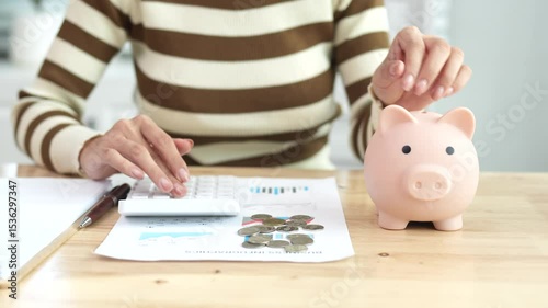 An Asian woman is putting money in a piggy bank while looking at a calculator, giving advice on financial planning.