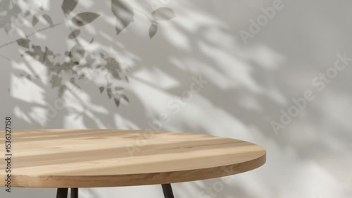 Wooden round table with leaf shadows on gray wall