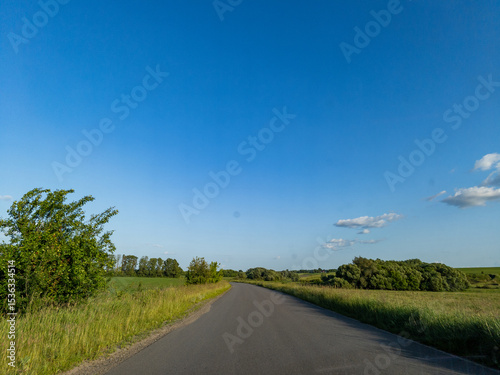 A country road in the middle of a grassy field under a blue sky photo