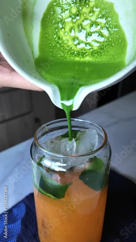 Closeup shot pouring matcha green tea into orange juice glass healthy fresh drink concept