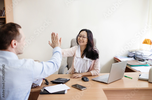 Two busy professional business people working in office with computer. Middle aged Asian female executive manager talking to male colleague having conversation showing software online solution.