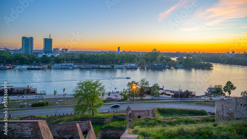 The Sava River gracefully flows past Kalamegdan fortress in Belgrade, Serbia, as the sun sets, casting vibrant colors across the sky and illuminating the tranquil water.