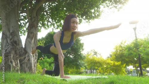 Young asian woman in sportswear stretching on a gym mat with a water bottle in a park, doing yoga. The young woman is taking care of her physical and mental health, wellbeing concept.