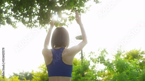 Back view of sports beautiful asian woman warming up outdoors, Asian woman doing yoga exercises, Fitness woman doing stretch exercise stretching her arms, wellbeing concept.