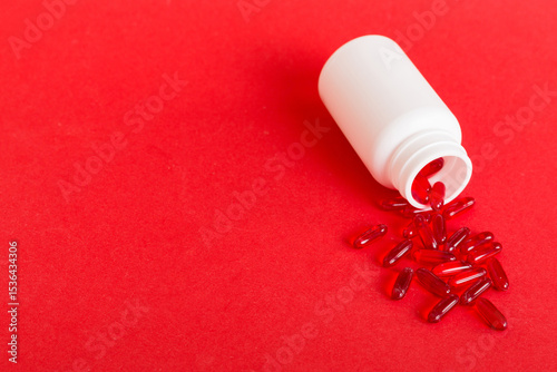 Red pills spilled around a pill bottle. Medicines and prescription pills flat lay background. Red medical capsules