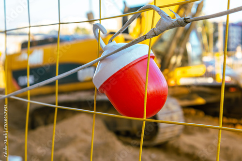 Red signal lantern on mesh fence around construction site. On long background construction equipment