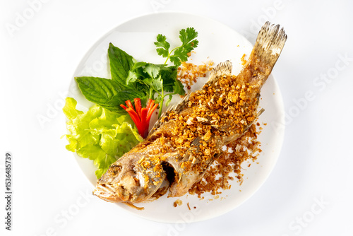 Fried sea bass sprinkled with Chinese garlic Fried until golden crisp, in a white dish,  on a  table.