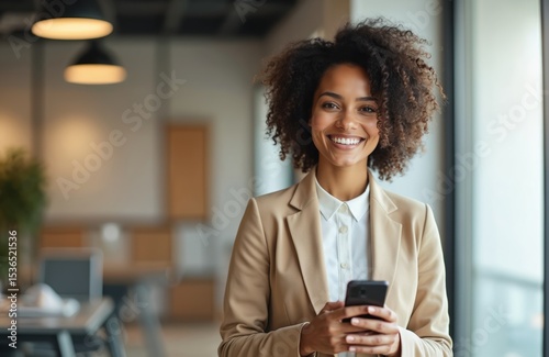 Attractive black business woman uses smartphone smiling in modern office. Pro female entrepreneur holds phone, texting, happy during work break. Business, technology, communication, corporate