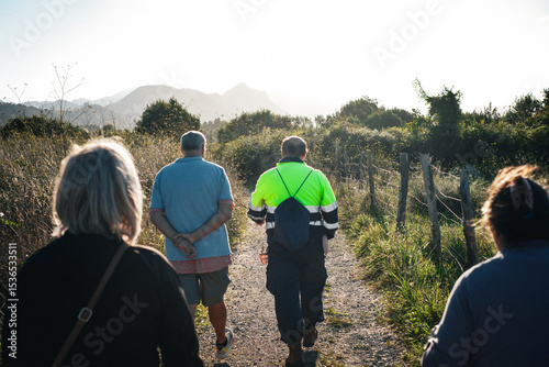 Un gruppo di persone cammina lungo un sentiero sterrato immerso nella natura, con vegetazione lussureggiante e montagne all'orizzonte