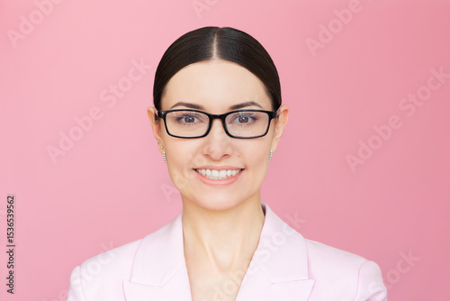 Portrait of young pretty Caucasian businesswoman wearing glasses and a pink suit on a pink background looking at camera and smiling