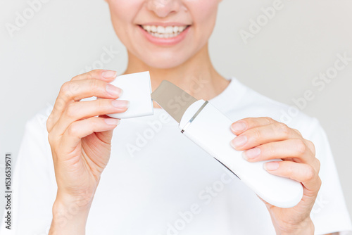 Young Beautiful Caucasian brunette woman in white clothes using a white ultrasonic facial cleaning device. Skin care.