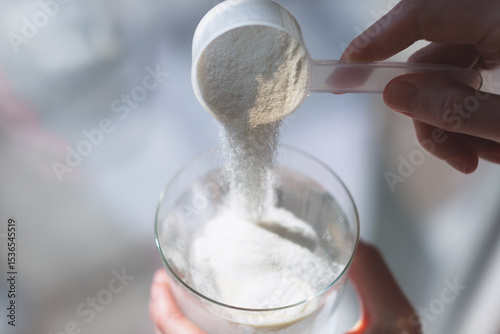 Woman hands with a scoop pouring collagen or protein powder in a glass of water. Trendy beauty supplement for healthy skin and bones.