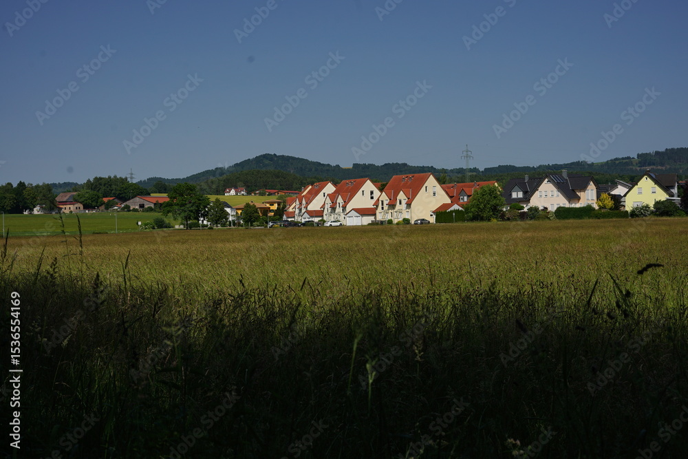 Obraz premium A residential area with uniform houses and red roofs set against green hills. This countryside scene emphasizes the calmness of life away from urban noise