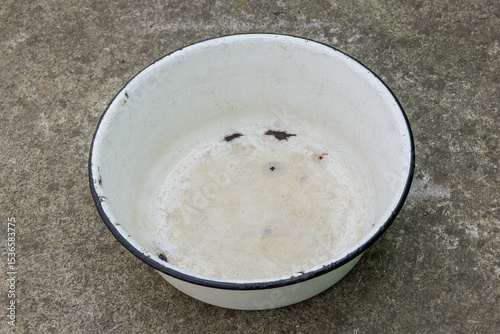 Worn enameled white basin with black rim on concrete ground outdoors