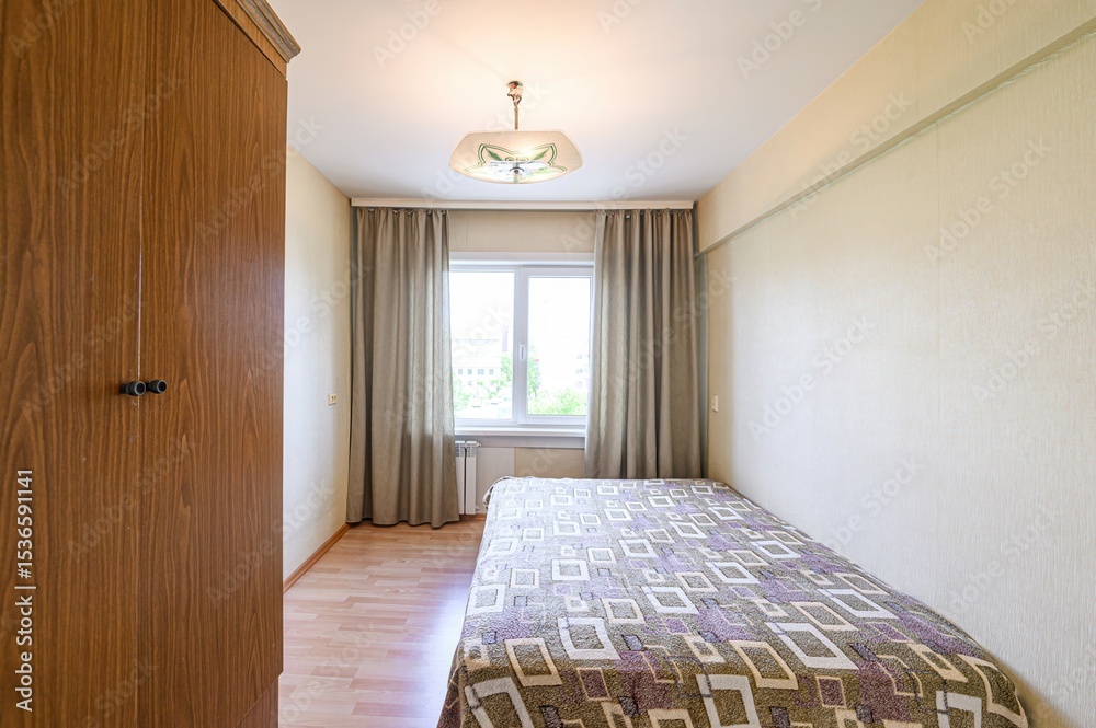 Obraz premium small, cozy bedroom with a single bed, wooden wardrobe, window with curtains, and a simple ceiling light