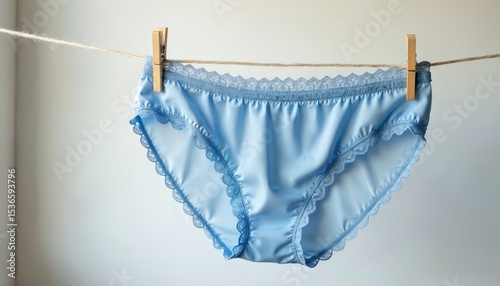 Delicate blue panties hang on clothesline against white background. Lingerie, lace detail, soft light. Underwear drying after washing at home, simple still life. Feminine design, clothing concept,
