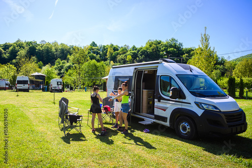 Family camping with a campervan in a campsite in Bosnia near Una River. Family relaxing with camper van, chairs and table on vacation, applying sunscreen before hike.