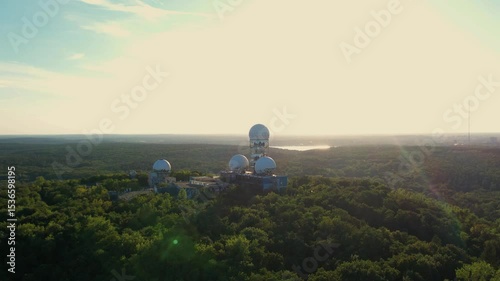 Aerial view of radar domes at sunset rising above a forest landscape with fields in the background