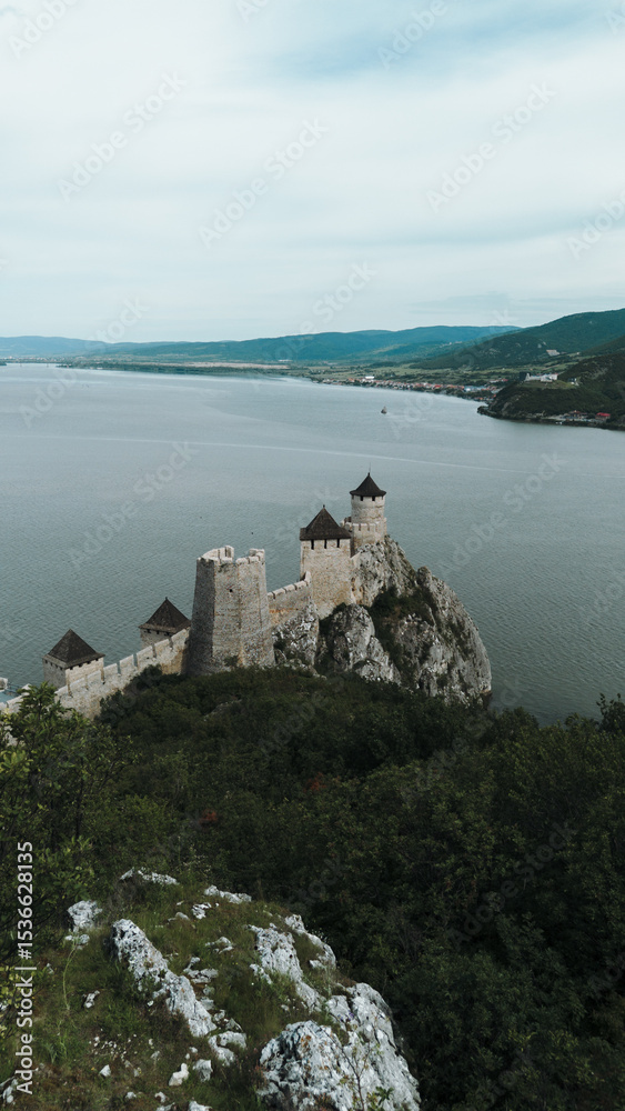 Naklejka premium Aerial view of Golubac Fortress on rocky cliff above the Danube River in Serbia, surrounded by water and medieval towers. The most popular and beautiful fortress in Serbia on the border with Romania