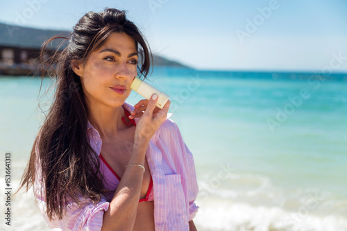 Beautiful Woman applying spf sunscreen stick on a sea background
