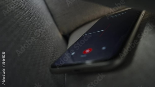 Smart phone with voice recording application is covertly grabbing conversation. Mobile phone hidden under and between couch or sofa pillows or bed. Wiretapping app or surveillance evidence gathering