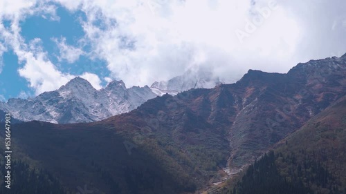 Clouds above snowy Himalayan mountain peaks during the summer season as seen from Sangla village in Kinnaur district, Himachal Pradesh, India. Scenic view of the mountains in summer season.
