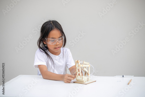 Фототапет A young girl learns basic engineering by playing with a hydraulic excavator toy
