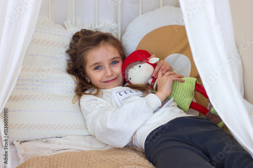 Cute little girl on bed hugging her favorite doll and smiling