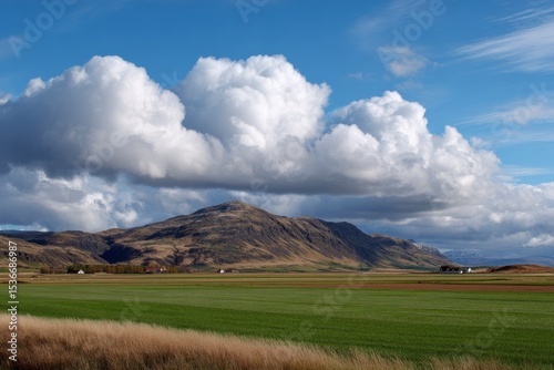 Verdant field before hills under cloudscape with blue sky