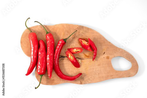 Top view of a collection of whole and sliced big red chilies arranged on a wooden cutting board, isolated on a white background