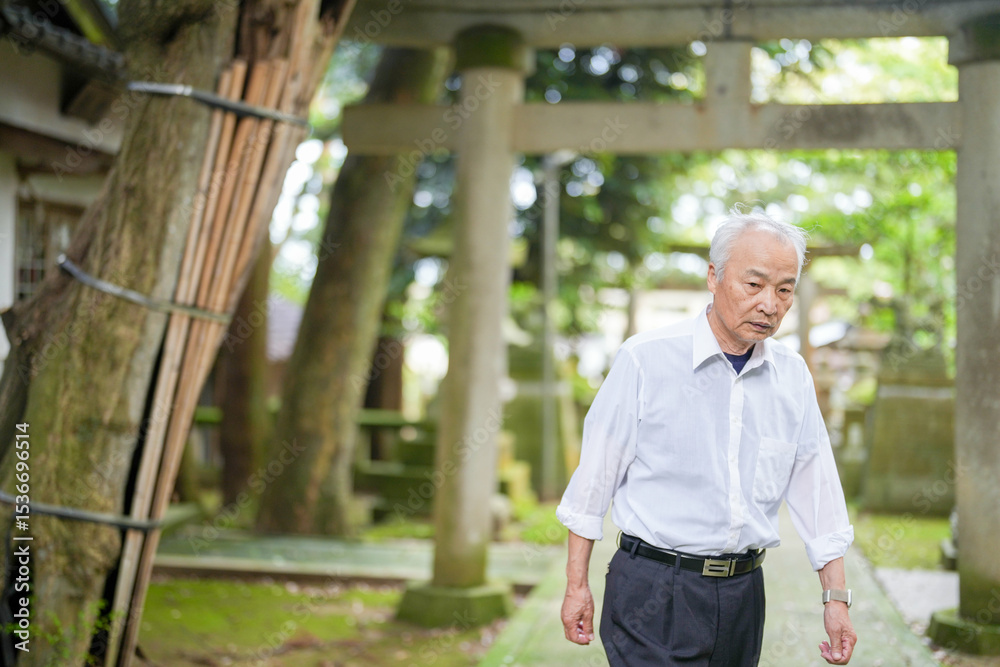 In rural Japan, a Japanese man in his late 70s visits a countryside shrine surrounded by lush green trees. Wearing a white shirt and hat, he prays quietly in the peaceful warmth of early summer air. In rural Japan, a Japanese man in his late 70s visits a countryside shrine surrounded by lush green trees. Wearing a white shirt and hat, he prays quietly in the peaceful warmth of early summer air.
