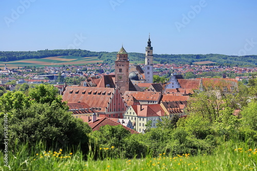 Luftaufnahme von Donauwörth mit roten Dächern, historischen Gebäuden und einem markanten Turm, eingebettet in eine grüne Landschaft. Die Stadt bietet eine charmante Kulisse.