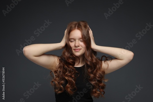 Beautiful teenage girl with healthy wavy hair on dark grey background